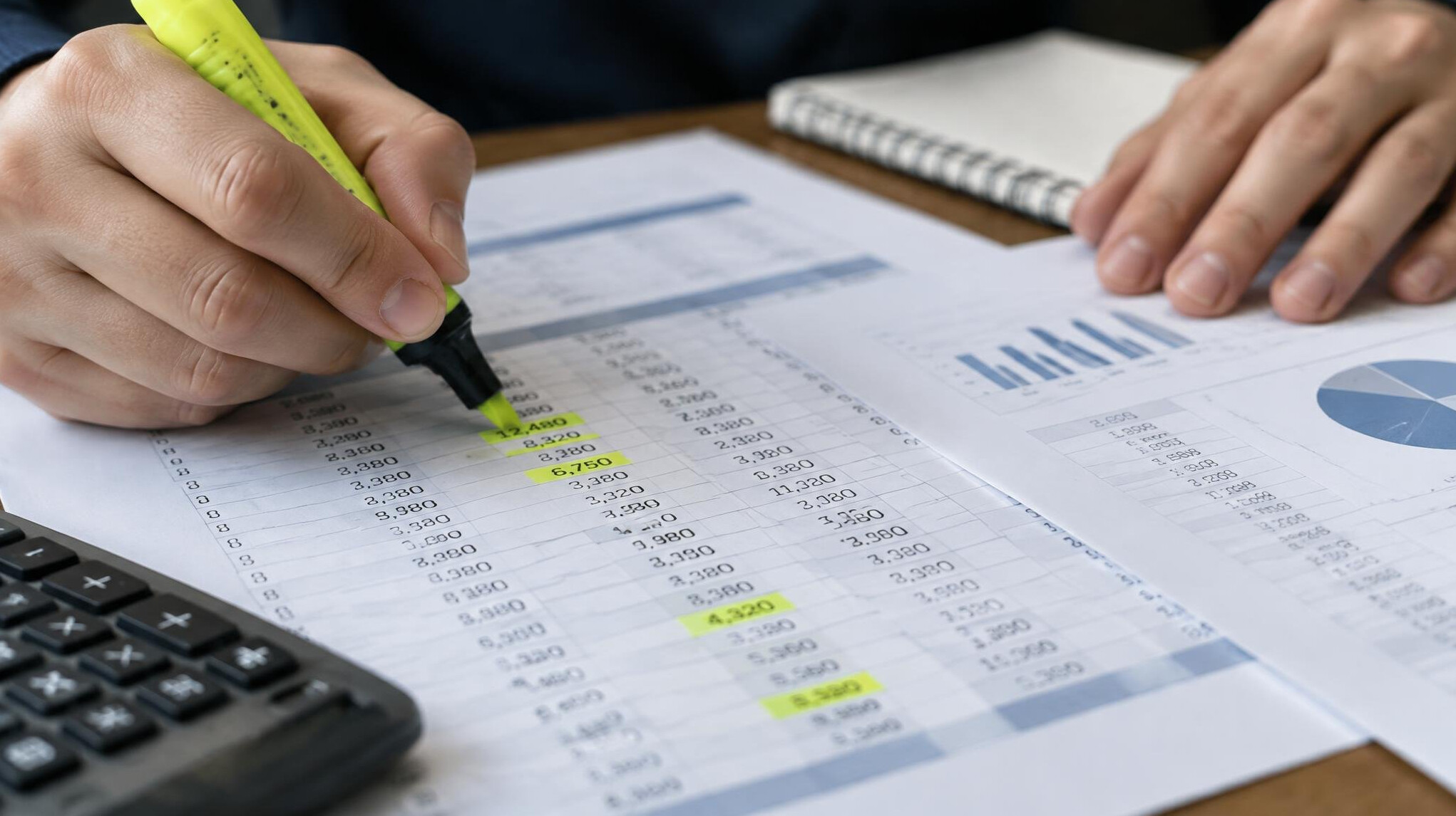 Close-up of hands reviewing a ledger and financial spreadsheet printouts